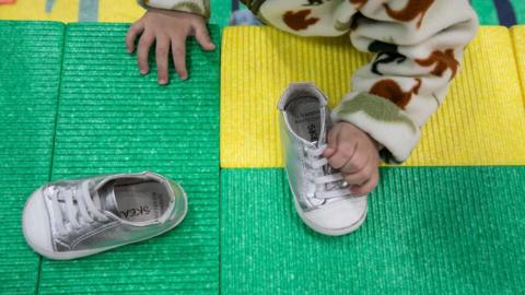 Close-up of a baby's hand grabbing a silver baby shoe. The baby is wearing a furry sweater.