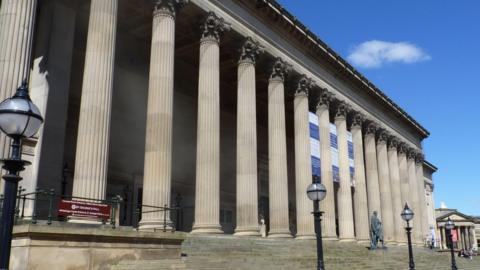 The exterior of St George's Hall in Liverpool is made up of at least fourteen columns with stone steps in front of them.