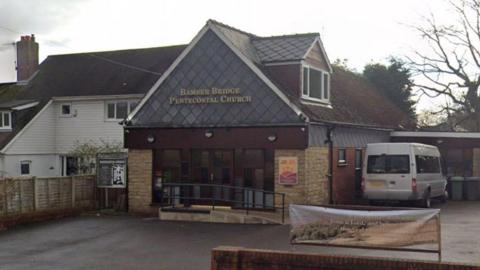 An image of a low-rise church building with minibus parked to the right hand side