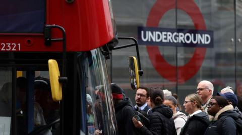 File image showing commuters attempting to board a red London bus outside Victoria train station in London in 2022, with the underground roundel visible in the background