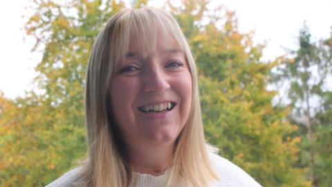 Image of Andrea Warnes smiling at the camera. She has short blonde hair, blue eyes, and is wearing a white jumper. 