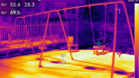 Thermal image of a playground and swings showing a hot yellow floor.