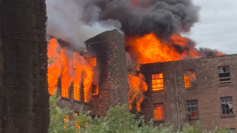 Image shows flames and smoke coming out of the red-brick, 19th-century Hotspur Press building in Manchester. 