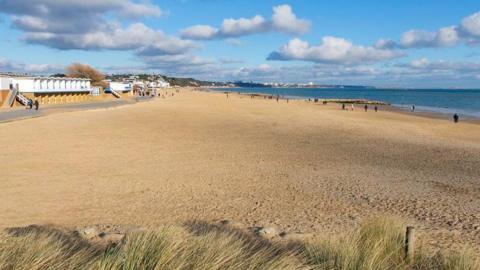Sandbanks beach with light coloured sand and blue sea. White buildings and people can be seen in the background