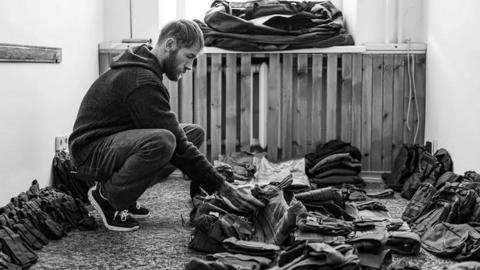 Chris Garrett, a man who has stubble and long light hair is crouched down looking at equipment.