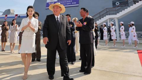 Kim Jong Un and his daughter Kim Ju Ae walk past honor guards with a destroyer in the background