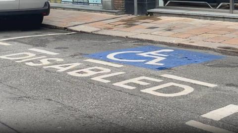 A picture of a blue painted disabled space on a roadside. You can see granite pavement in the background. 