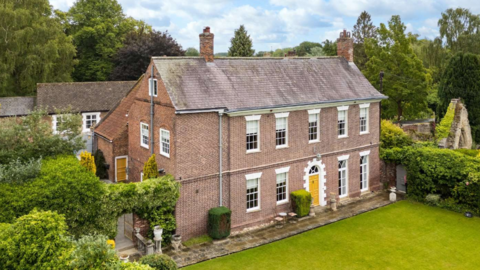 A large stone detached house with surrounded by green hedges and lawns