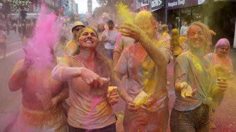 Four people throwing coloured paint powder into the air. They are covered in it and smiling. 
