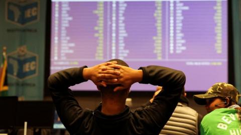 A member of the Patriotic Alliance political party looks at an electronic board where results of the South African national election are displayed at the Western Cape Independent Electoral Commission Results Operating Centre, in Cape Town, South Africa, May 30, 2024