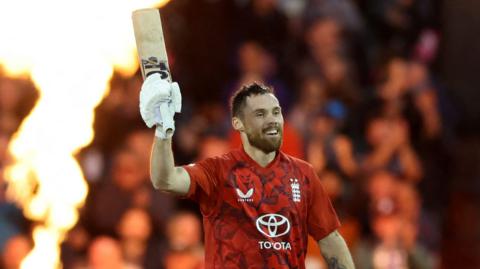 Phil Salt celebrates a century but raising his bat, with fireworks in the background