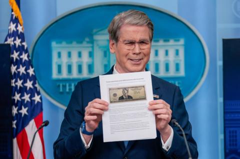 A man with short, grey hair holds up a piece of paper with a note on it