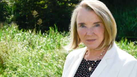 Irene Walsh wearing a black blouse with red and white dots and a white blazer on top