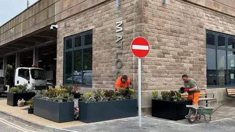 Workers in high vis planting up newly-installed planters outside the transport hub