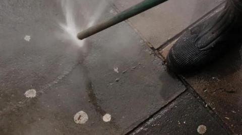 A street cleaner hoses chewing gum from a pavement 