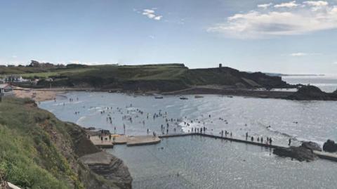 A view of Summerleaze Beach including a bathing pool. Lots of people are in the water