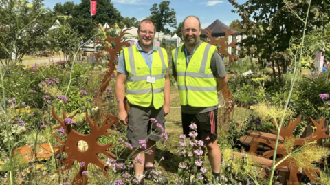 Two men in a garden wearing hi-vis. 