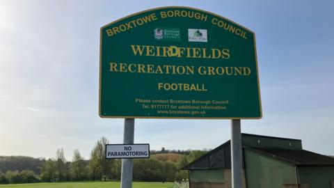 A big green sign on a sunny day. It reads 'Weir Fields Recreation Ground', a smaller sign sits below it and says 'No Paramotoring'.