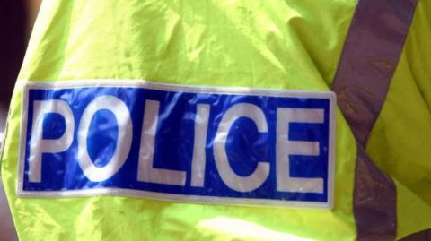 A generic image of the back of a police officer, who is wearing yellow. The word police is in white on a blue background