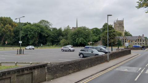 A car park with trees and church nearby
