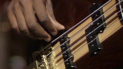 A closeup of a hand playing a bass guitar