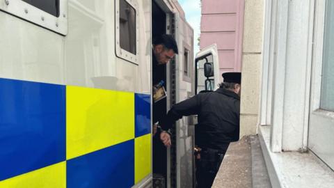 Dylan Pounds being led out of a police van into Jersey's Royal Court while handcuffed to an officer.