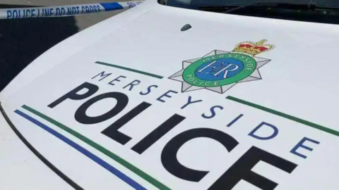 Stock shot of the bonnet of a Merseyside Police van, which is white. The text 'MERSEYSIDE POLICE' is seen on the front in black and blue lettering.