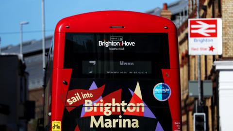 The back of a red bus with sail into Brighton Marina on the back