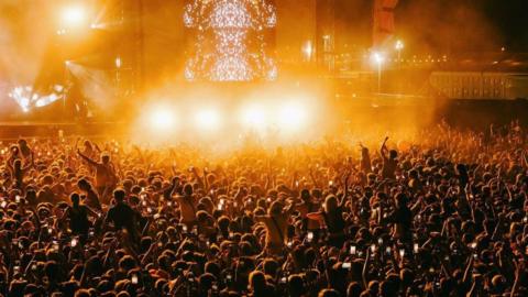 A large crowd of festival goers watching a band on stage at night with their hands in the air