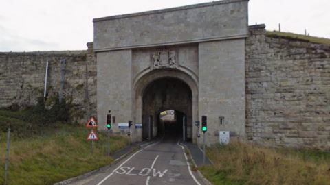 Google street view of an archway entrance on a road with traffic signals in front of it 