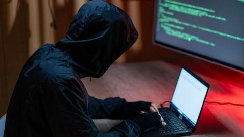 A man in dark clothing posing as a cyber-criminal
