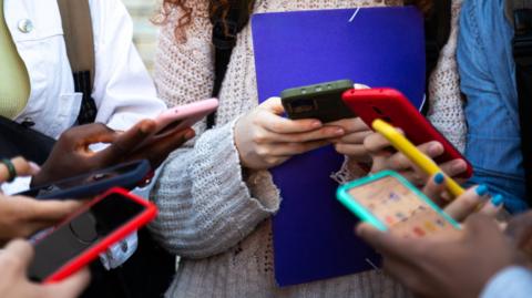 Students stand in a circle on their smart phones in a stock photo