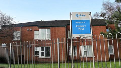 The outside railings of the fold. The building is red brick and a blue and white sign is at the front which says Inverary Fold in white letters.