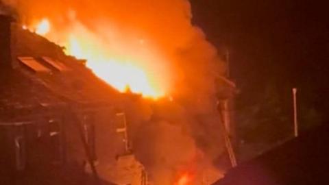 Flames coming out of the roof of a house during the night