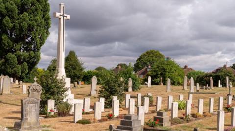 A photo of Gloucester Old Cemetery showing rows of gravestones and a tall stone cross.