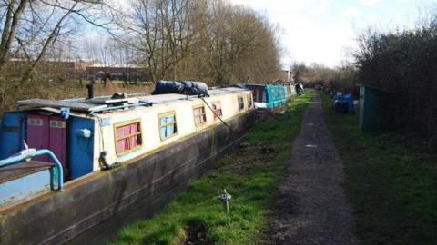 Canal boats lined-up along the Oxford Canal, with a towpath next to the water.