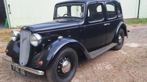 A refurbished, black 1938 Austin 10 Cambridge parked outside a garage.