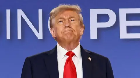 Donald Trump attends a press conference, wearing a red tie, white shirt and navy suit