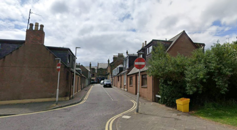 A terraced residential street with No Entry signs and a grassy area with trees to the right of the photo.