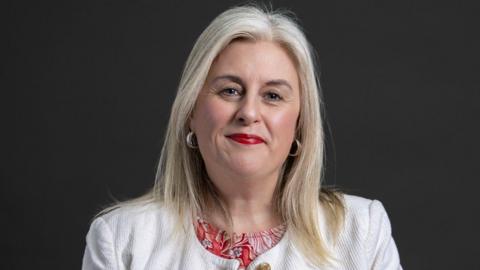 A woman with light hair in a white jacket.