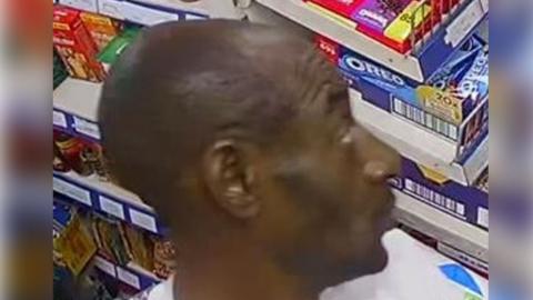 A man standing in front of a row of shelves in a store.