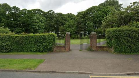 The entrance gates to Northwood Park. Bushes and trees can be seen either side.