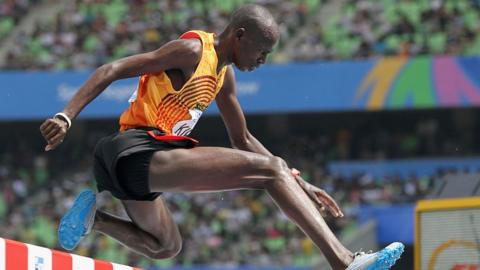 A side view of Benjamin Kiplagat leaping over a hurdle.