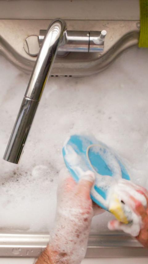 Hands clean a blue plate in soapy water in a sink.