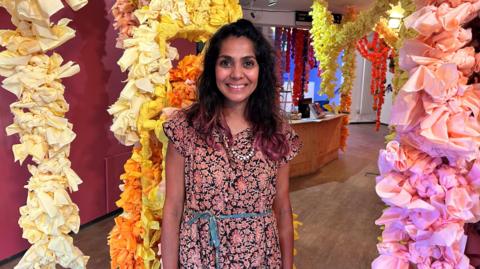 Saroj Patel at her exhibition space, surrounded by colourful Indian decorations.