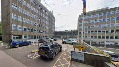 a car park with two concrete six-storey buildings either side and a flag in the foreground 