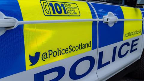 A close up of a police car. The vehicle is decorated with blocks of yellow, blue and white colours and has information on how the public can contact police and follow Police Scotland on social media.