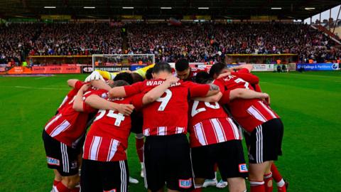 Exeter City players in a huddle in front of the Big Bank