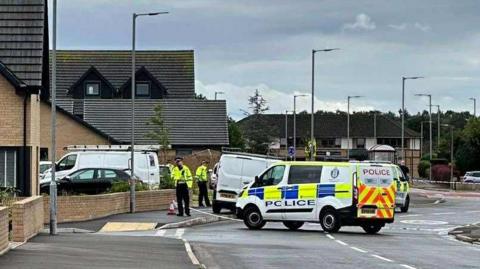 A cordoned off street with police cars gathered round and officers standing nearby
