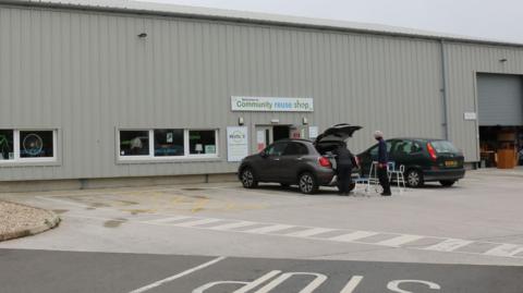 A grey industrial building with a couple of cars parked outside